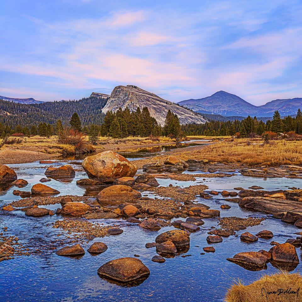 A faint pastel glow illuminates the clouds above Lembert Dome and Tuolumne Meadows at sunset, as the Tuolumne River begins to freeze over as winter approaches.