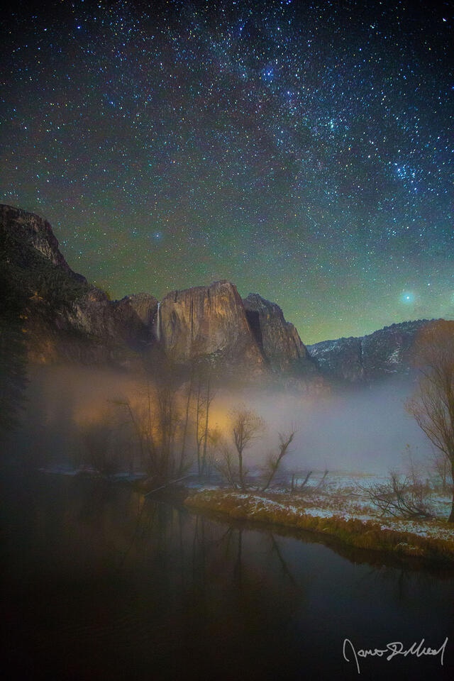 Soft fog rises up, blanketing the valley floor and the Merced River of Yosemite Valley in a fine mist while Yosemite Falls plunges over the cliffs high above.