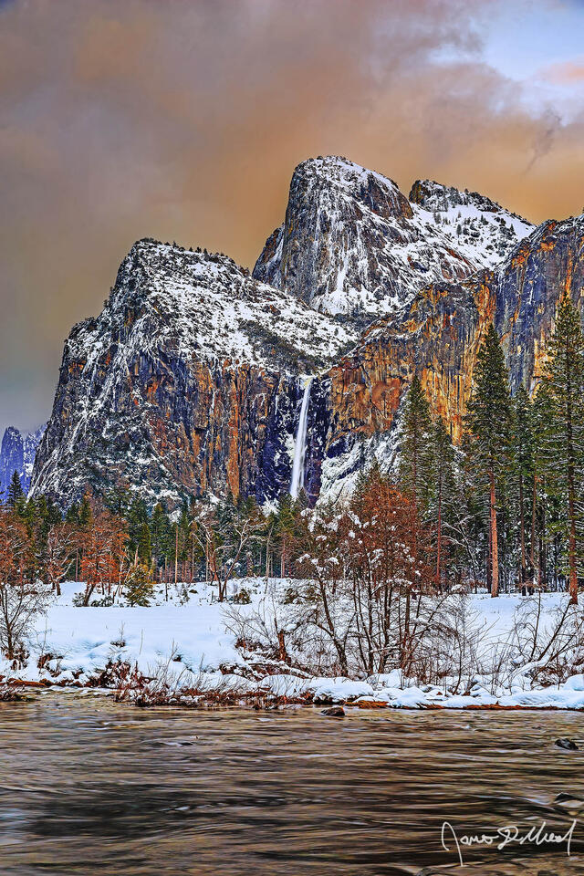 Sunset lights the clouds above the Merced River and Cathedral Rocks as Bridalviel Fall tumbles over the cliffs towards snow covered Yosemite Valley 