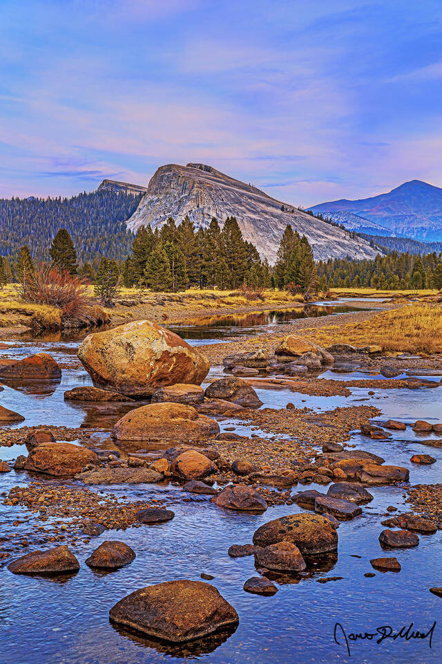 A faint pastel glow lights the clouds above Lembert Dome and Tuolumne Meadows at sunset. Glacial Erratics line the Tuolumne River as it begins to freeze over