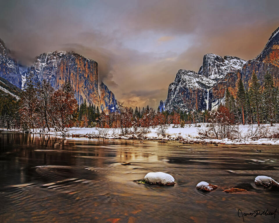The full moon rises at Sunset behind the clouds as color from the setting sun lights the sky, as El Capitan & Cathedral Rocks rise high above the Merced River.