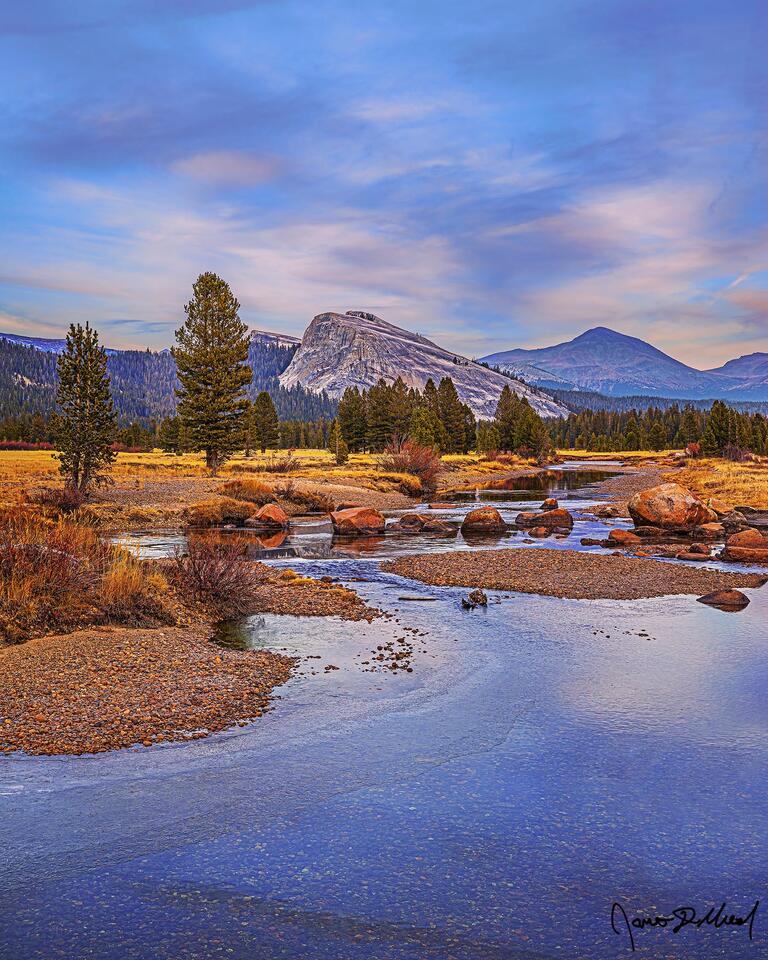 The Tuolumne River begins to freeze over for the winter in Tuolumne Meadows; colors of sunset light the clouds above Lembert Dome, Dog Dome and Mount Dana.