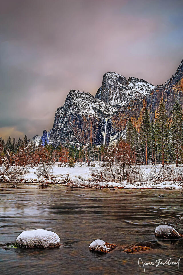 Alpenglow lights the clouds above the Merced River and Cathedral Rocks as Bridalviel Fall tumbles over the granite cliffs towards snow covered Yosemite Valley