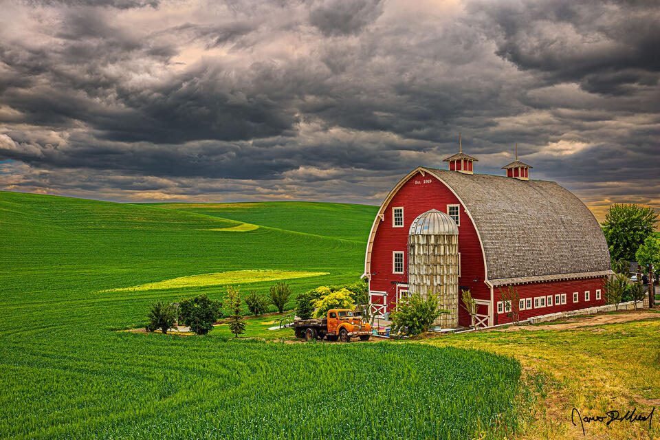 Storm clouds above the Heidenreich Dairy Barn in the Palouse filter sunlight onto the surrounding fields.
