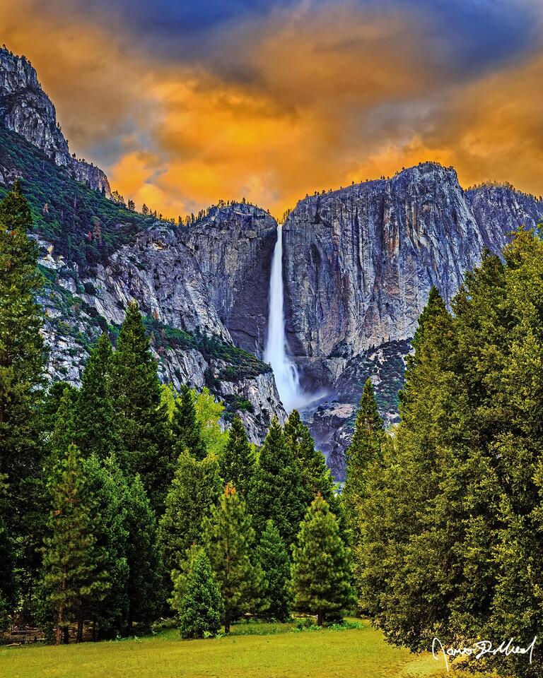 Sunset over Yosemite Falls lights the clouds in the skies above Yosemite Valley a fiery orange as the waterfall tumbles over the cliffs towards the valley below