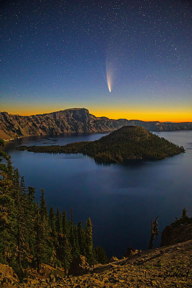 As Nautical Dawn approaches, moonlight illuminates Crater Lake and Wizard Island while Comet NEOWISE streaks across the quiet morning sky.