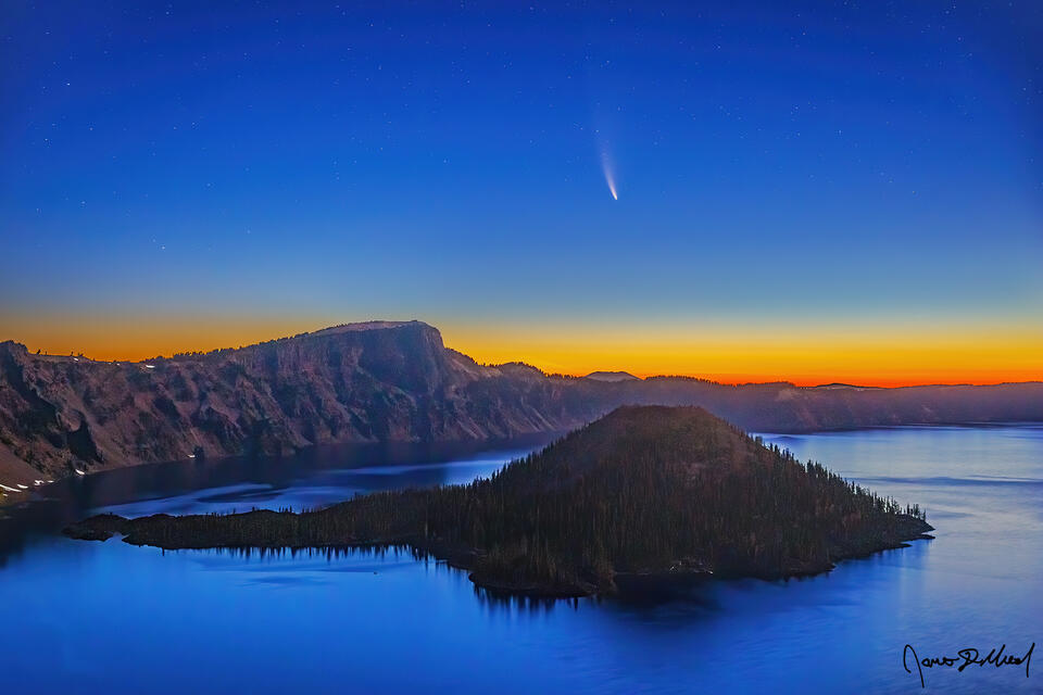 As nautical dawn takes hold, Comet NEOWISE fades into the horizon above Wizard Island and Crater Lake while the first hints of sunrise color the eastern sky.