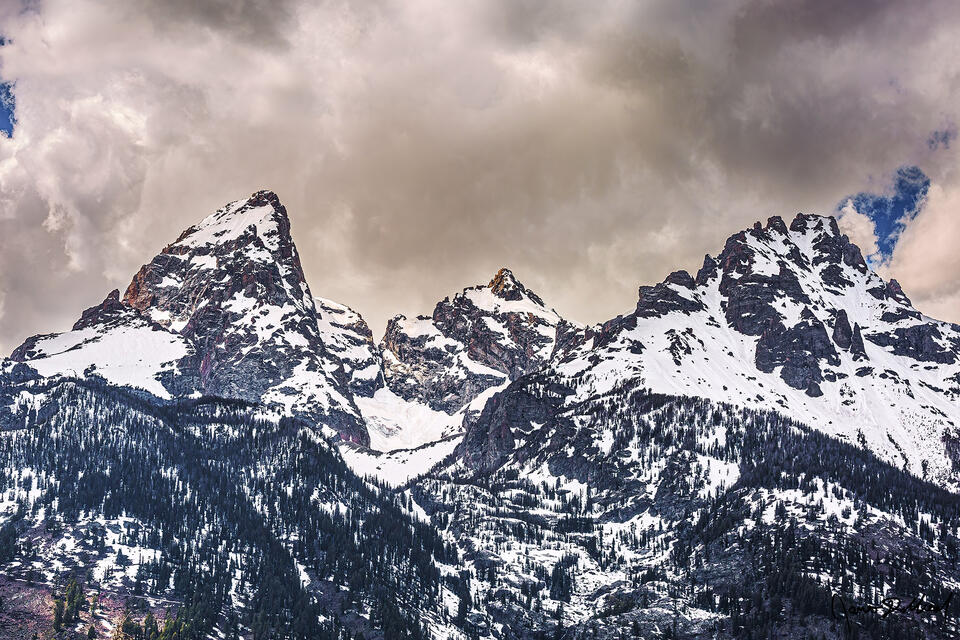 Clouds blanket the skies above the Grand Teton, Mount Owen and Teewinot Mountain as the peaks rise up into the sky like cathedral spires made of snow and stone.