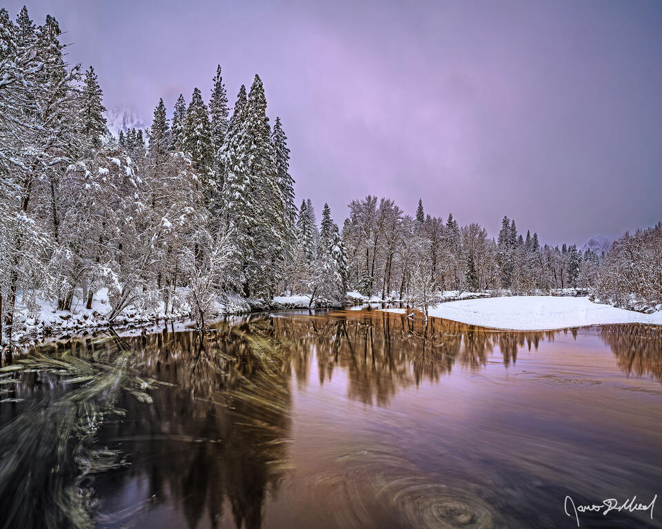 Alpenglow at sunset illuminates a veil of fog covering the granite cliffs of Yosemite Valley as the scene reflects in the waters of the Merced River.