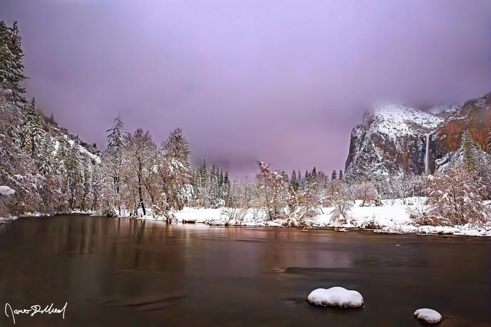 Clouds and fog envelope Cathedral Rocks above Yosemite Valley and the Merced River while alpenglow and the rising begins to illuminate the clouds on the horizon