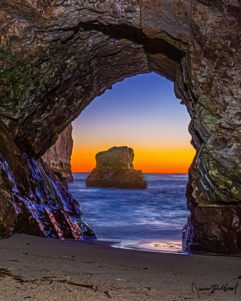 A view through an opening of a sea cave shows the colors of dusk setting in over the Pacific Ocean along the Pacific Coast of California