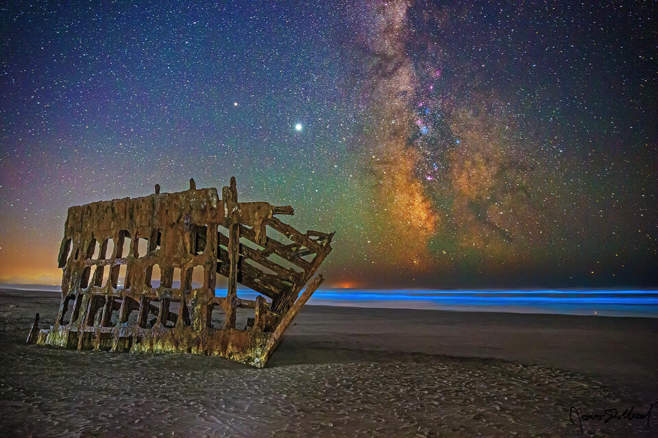 Bioluminescence illuminates the Pacific Ocean behind the Wreck of the Peter Iredale along the Oregon Coast as the Milky Way rises high into the sky above. 