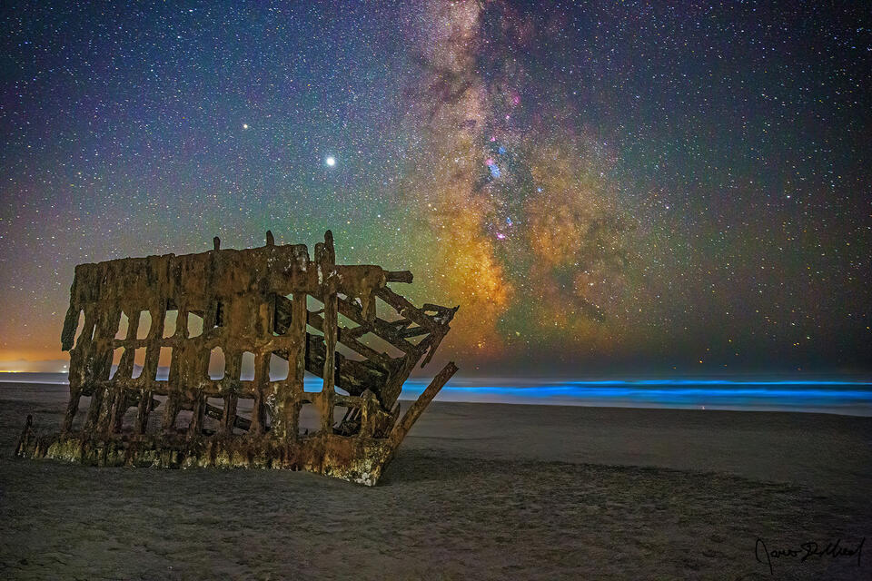 Bioluminescence illuminates the Pacific Ocean behind the Wreck of the Peter Iredale along the Oregon Coast as the Milky Way rises high into the sky above.