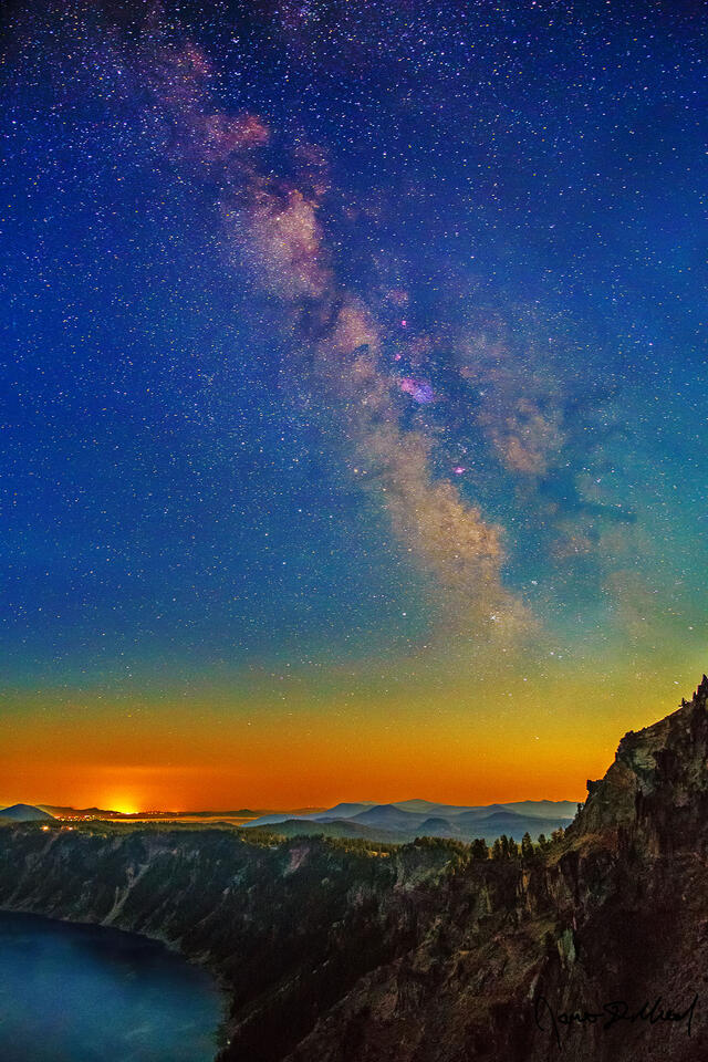 Light pollution from Klamath Falls looks like the sun rising on the horizon as the Milky Way rises above Crater Lake’s moonlit caldera rim.