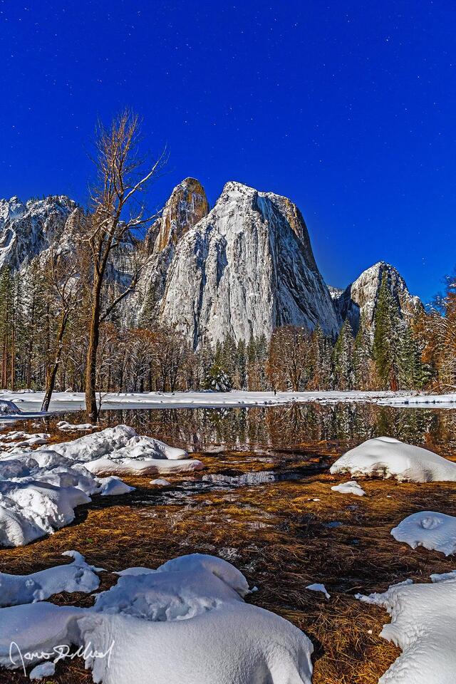 Moonlight illuminates Yosemite Valley as it lay covered in a blanket of deep snow. Cathedral Rocks and Spires reflect in the still waters of Wosky Pond 