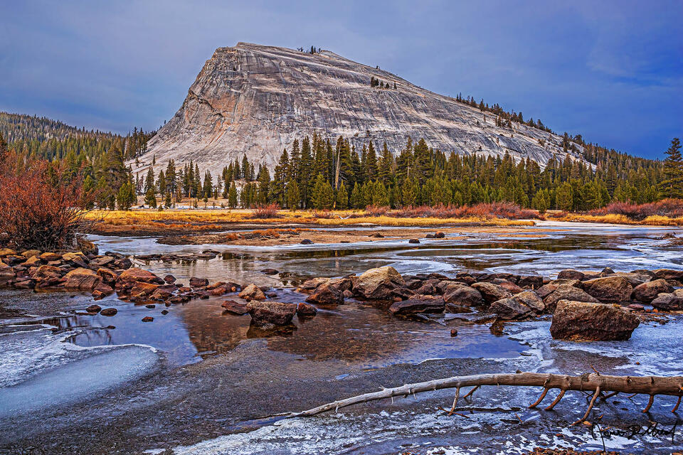 The Tuolumne River begins to freeze over after a cold spell as the first storm of winter nears; Lembert Dome reflects in the small patches of unfrozen water.