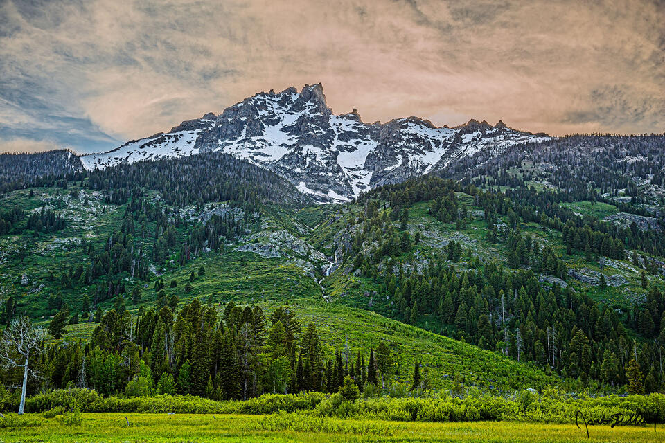 Rays from the setting sun illuminate the northern face of Teewinot Mountain as Broken Falls tumbles 300 feet towards Lupine Meadows below.