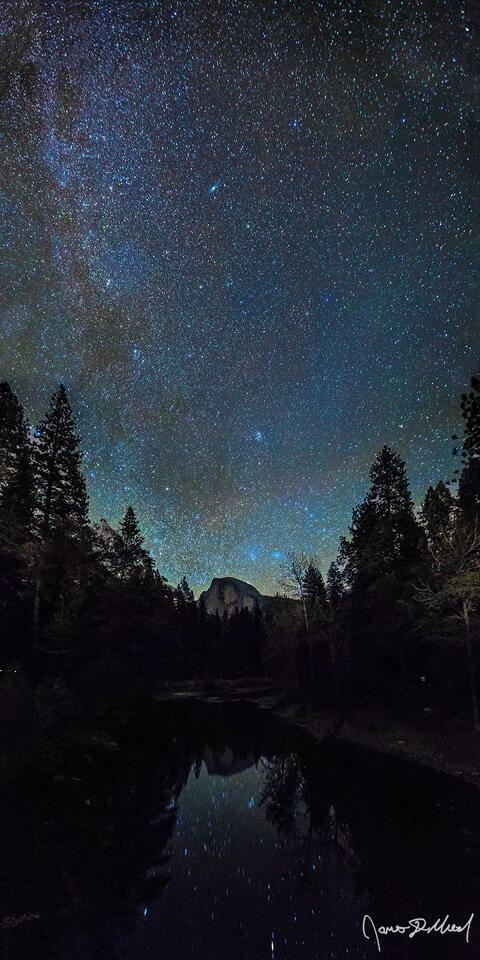 The Milky Way rises into the sky above Yosemite Valley as Half Dome and the stars in the sky reflect off the still waters of the Merced River below.