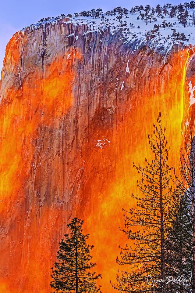 Sunset lights the waters of Horsetail Fall orange like Lava. Wind kicks up mist, pulling it across El Capitan as the famous Yosemite Firefall comes to life.