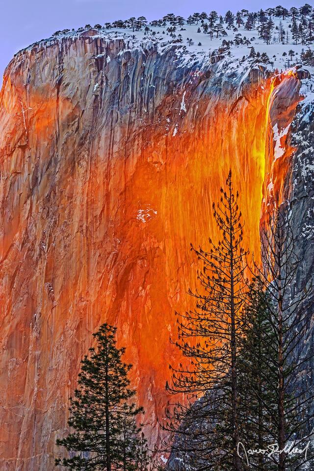 Sunset lights the water of Horsetail Fall orange like Lava. Wind kicks up spray, pulling it across the face of El Capitan as the Yosemite Firefall comes to life