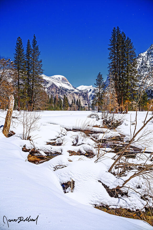 Yosemite Valley lays covered in a deep blanket of winter snow as moonlight illuminates North Dome, Royal Arches and the night sky above.