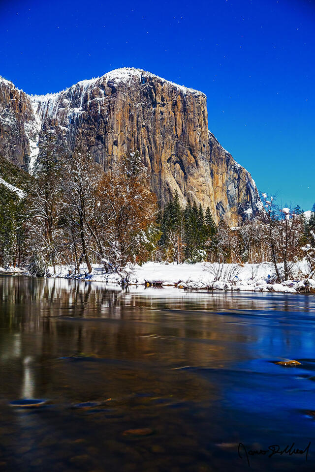 Moonlight illuminates Yosemite Valley, El Capitan, and the Merced River in the winter as snow blankets the valley on a cold winter night.