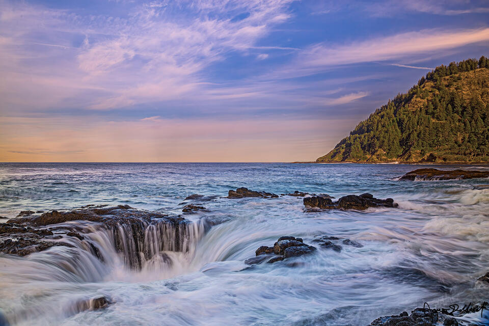 Sunset lights the clouds as waves of the Pacific Ocean crash into the headlands at Cape Perpetua and drain down into Thor's Well during a 10.20 foot King Tide 