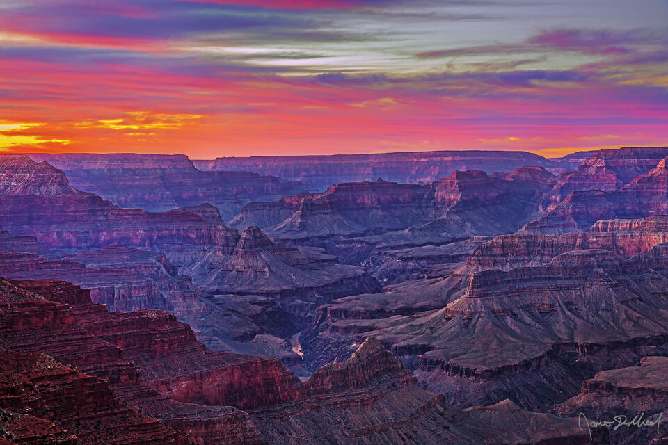 Sunset over the Grand Canyon and the Colorado River brings a warm glow to the clouds in the sky as the red colors of the canyon's temples and walls come to life