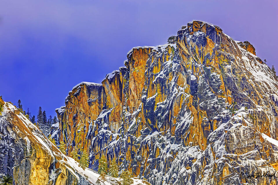 Winter snow covers the slopes and the tops of a ridge over 3300 feet above the Yosemite Valley floor as sunset bathes the granite cliffs high above.