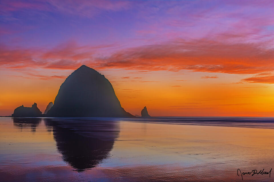 Haystack Rock stands like a silhouette against a canvas of pastel colors at sunset as it rises up over the Pacific Ocean.