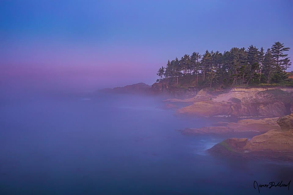 Fog covers the headlands near Depoe Bay and the waters of the Pacific Ocean as the pastel colors of dawn begin to show on the horizon.