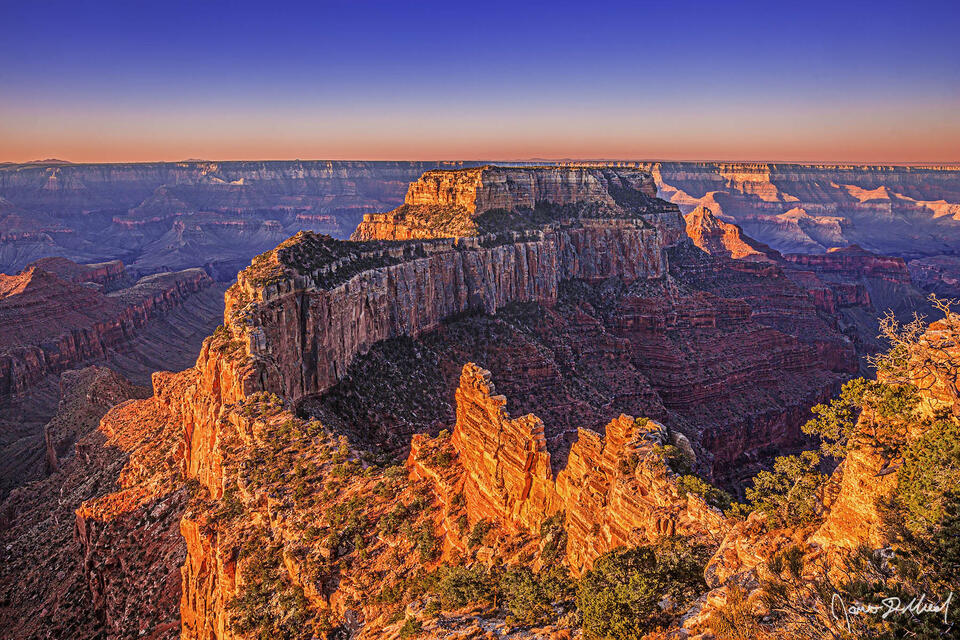 Sunrise casts a warm glow onto Wotan's Throne, Cape Royal and the south rim of the Grand Canyon in the distance as a new day begins.