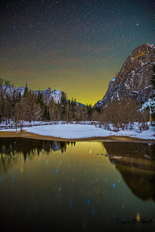 Lower Brother, Cathedral Rocks and snow covered Yosemite Valley reflect in the still, cold waters of the Merced River as the stars in the night sky shine bright