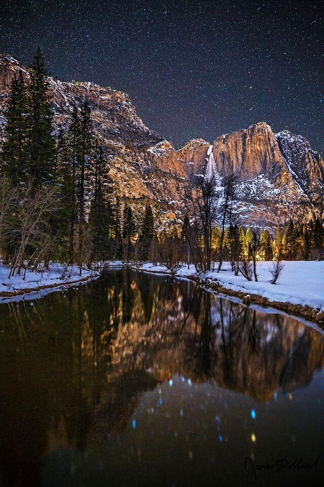 Yosemite Falls tumbles 2425 feet over the cliffs towards snow covered Yosemite Valley below as the scene reflects in the cold, still waters of the Merced River.
