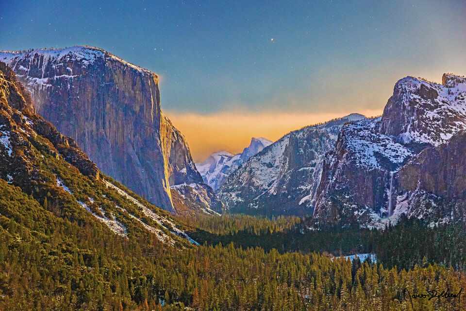 Winter moonlight illuminates the snow covered top of El Capitan, Half Dome and Cathedral Rocks and Spires as Bridalveil Fall flows 620 feet the cliffs.