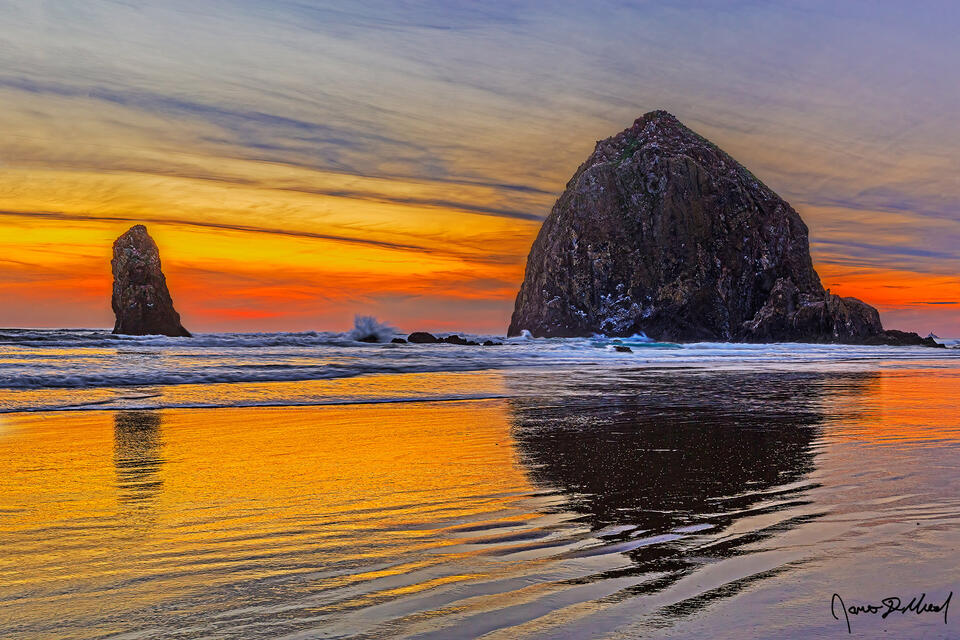 Sunset illuminates the skies over Haystack Rock, The Needles and the Pacific Ocean at Cannon Beach Oregon as the day draws to a close.