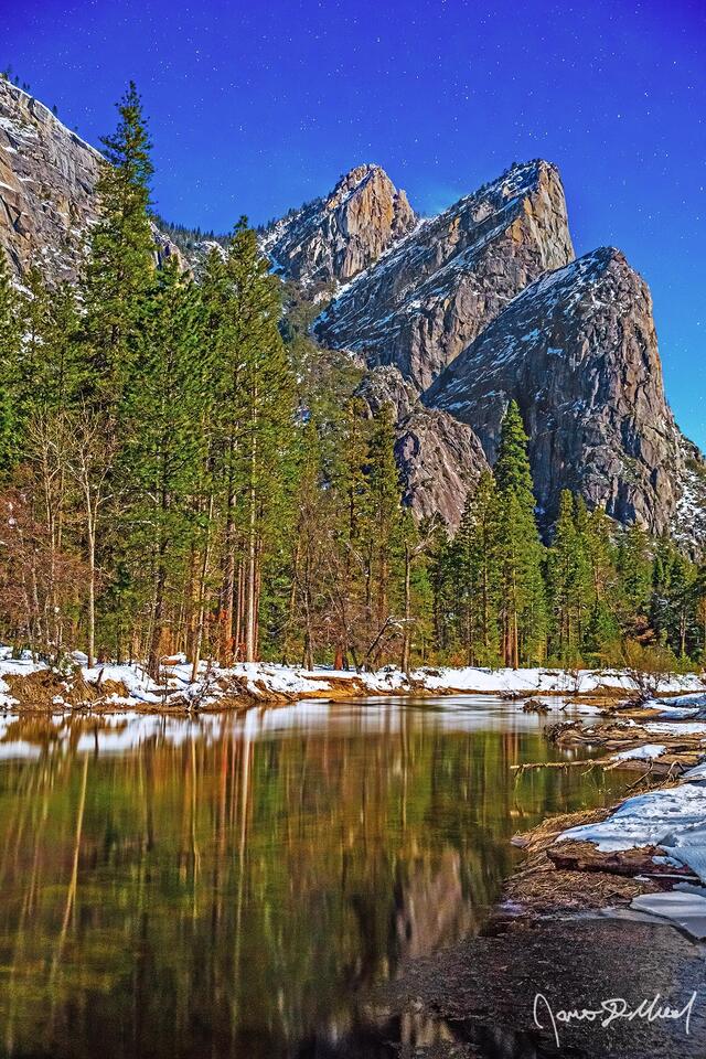 A full Moon illuminates the Three Brothers and the Merced River at midnight in the dead of winter. Fresh snowfall glows in the moonlight as it lines the shores.