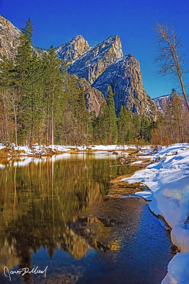 A full Moon illuminates the Three Brothers as they reflect in the Merced River at in the dead of winter. Fresh snowfall glows in the moonlight next to the river