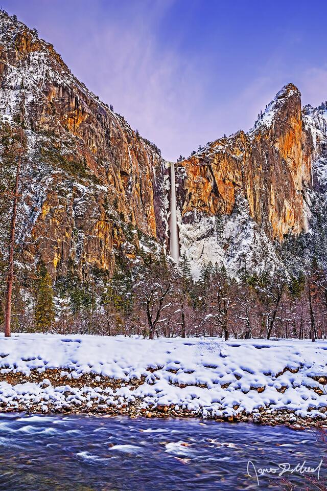 Sunset lights the clouds in the sky over Bridalveil Fall, The Leaning Tower, Bridalveil Meadow and the Merced River as snow blankets the meadows of Yosemite.