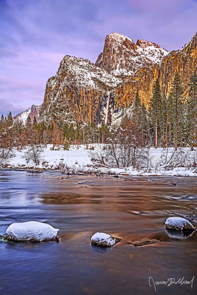 Alpenglow illuminates the skies above the Merced River and Cathedral Rocks as Bridalveil Fall tumbles over the cliffs towards snow covered Yosemite Valley below