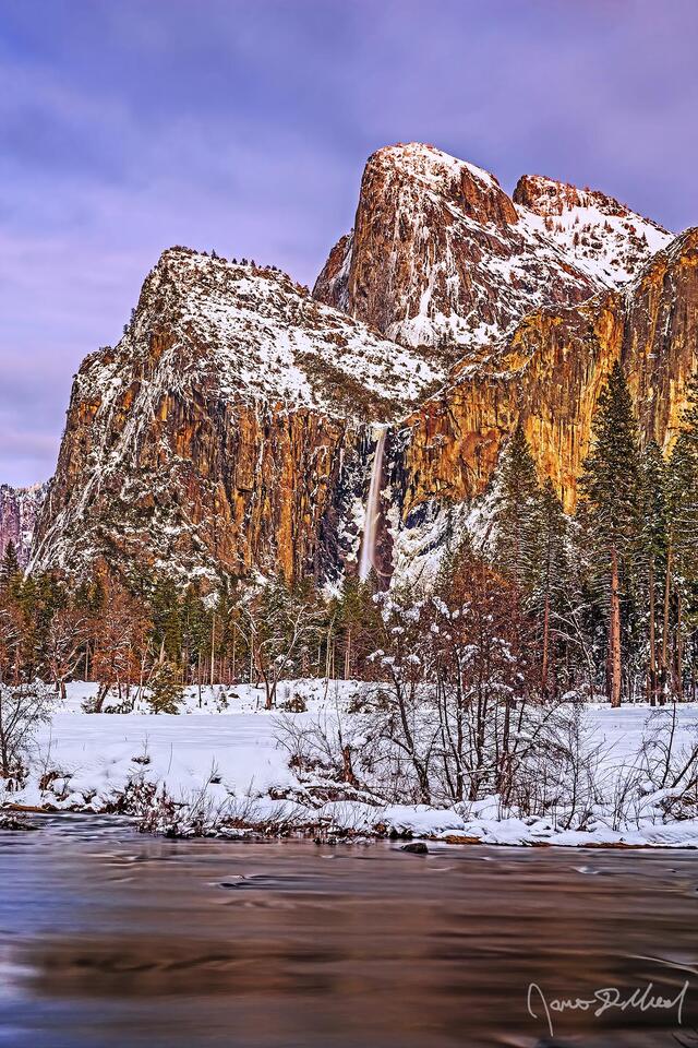 Alpenglow after sunset illuminates the skies above the Merced River and Cathedral Rocks as Bridalviel Fall tumbles over the cliffs towards snowy Yosemite Valley