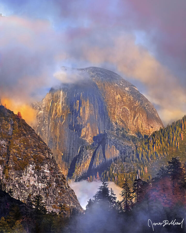 Clouds and fog begin to part at sunset as Half Dome comes into view, framed in a veil of clouds and fog as it rises high above the landscape below.