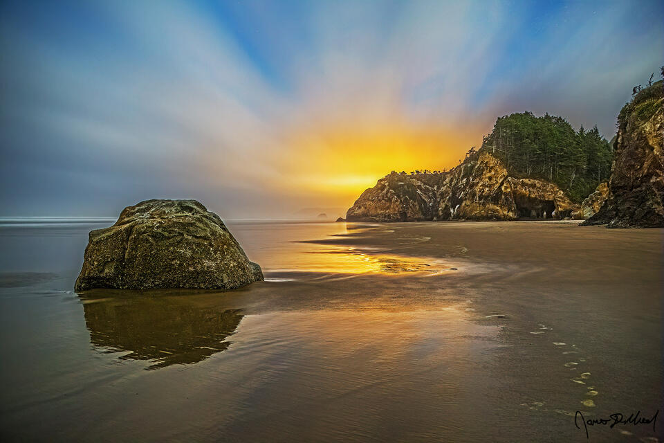 Low tide in the Pacific Ocean leaves the sand with a wet reflection out past Hug Point and Adair Point as light pollution creates a warm sunset like glow.