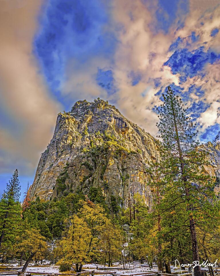 Sunset bathes the clouds above Cathedral Rocks in golden light as the first snow of late autumn blankets the Yosemite Valley floor.