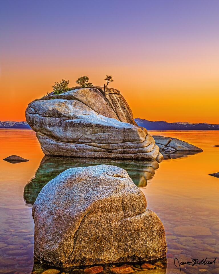 Sunset casts a golden glow off the waters of Lake Tahoe, as Bonsai Rock rises up from the clear, liquid gold water of the lake.