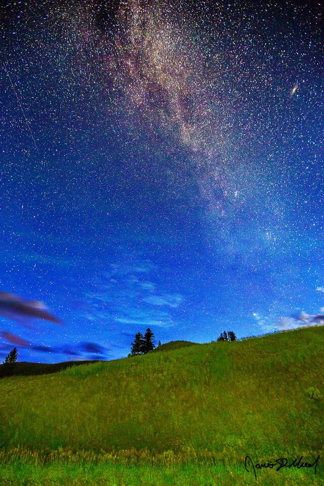 The Milky Way rises high into the sky above a rolling hillside while the greens of the Auroras fade, give way to blue colors as nautical dawn approaches.