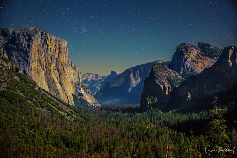 Moonlight bathes the cliffs of El Capitan, Cathedral Rocks and Half Dome at night above Tunnel View as Bridalveil Fall tumbles over the granite cliffs.