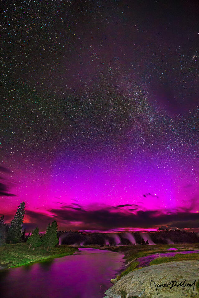 The Aurora Borealis reflects off the waters of the Firehole River while the Andromeda Galaxy rises high in the sky above Midway Geyser Basin in Yellowstone.