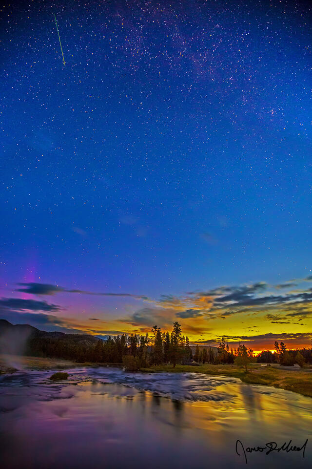 The last light of the Aurora Borealis dances above the Firehole River in Yellowstone as the first light nautical dawn begins to illuminate the morning skies.