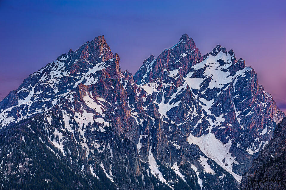 Pastel colors illuminate the sky at sunset as alpenglow illuminates the upper slopes of Teewinot Mountain, Grand Teton and Mount Owen (the Cathedral Group)